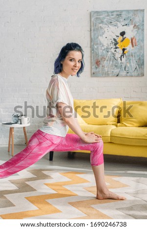 Girl with colorful hair doing yoga asana and looking at camera in living room