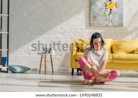 Girl with colorful hair touching leg on yoga mat in living room