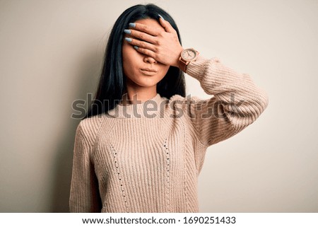 Young beautiful chinese woman wearing casual sweater over isolated white background covering eyes with hand, looking serious and sad. Sightless, hiding and rejection concept