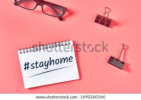 Paper notebook with hashtag stay home near binder and modern glasses on pink desk. Concept of quarantine