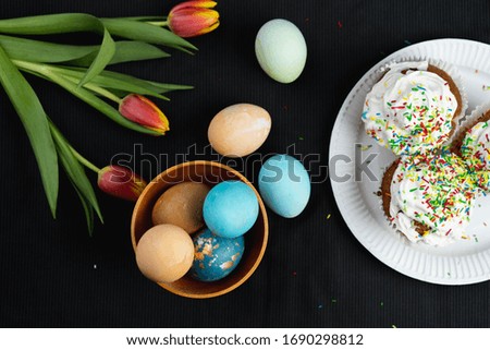 Black background, on it a white plate s Easter cakes, cream, decoration, tulips, eggs, decor.