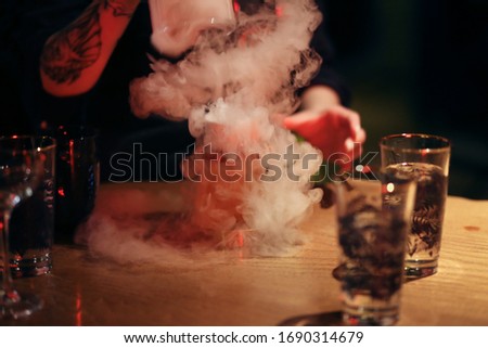 A pink and orange cocktail is served in the bar with smoke, a special wow effect. Dark bar, evening atmosphere, alcohol.
