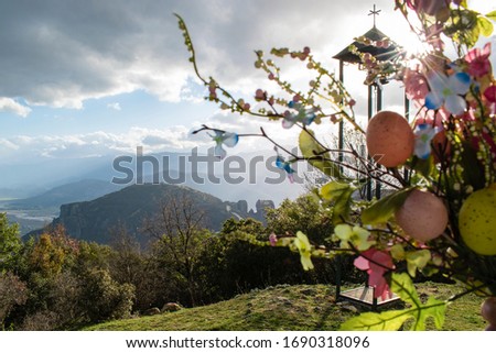 Easter landscape in Meteora, Greece. Flowers with coloured easter eggs bouquet near church bell