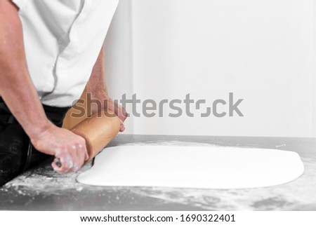 Woman using rolling pin preparing royal icing for cake decorating, hands detail .