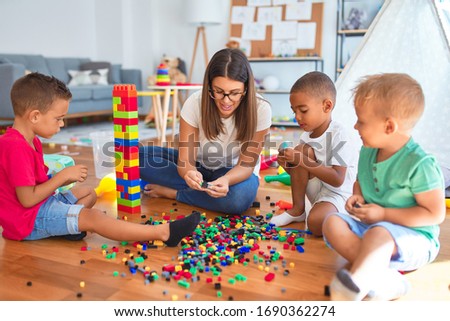 Young beautiful teacher and toddlers playing with building blocks around lots of toys at kindergarten Royalty-Free Stock Photo #1690362274