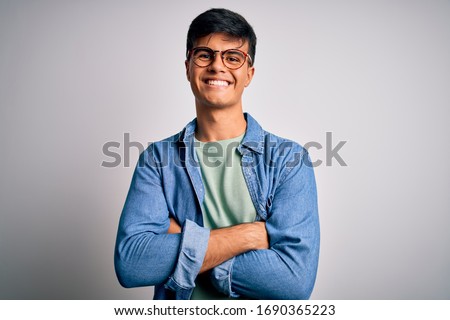 Young handsome man wearing casual shirt and glasses over isolated white background happy face smiling with crossed arms looking at the camera. Positive person.