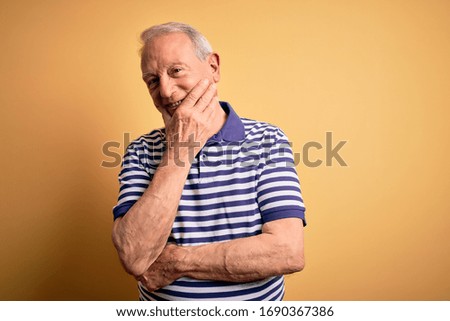 Grey haired senior man wearing casual navy striped t-shirt standing over yellow background looking confident at the camera smiling with crossed arms and hand raised on chin. Thinking positive.