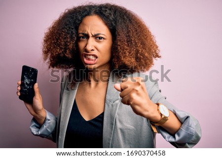 Young african american woman with afro hair holding cracked and broken smartphone screen annoyed and frustrated shouting with anger, crazy and yelling with raised hand, anger concept