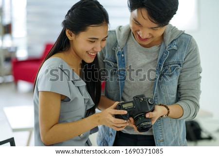 young handsome attractive man photographer displayed picture in  camera after  taking photo of beautiful model young asian woman in studio during COVID-19 pandemic working at home quarantine