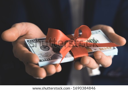 Concept, money as a gift, win or bonus. businessman takes or gives pile of 100 dollar bills tied with red ribbon with bow.