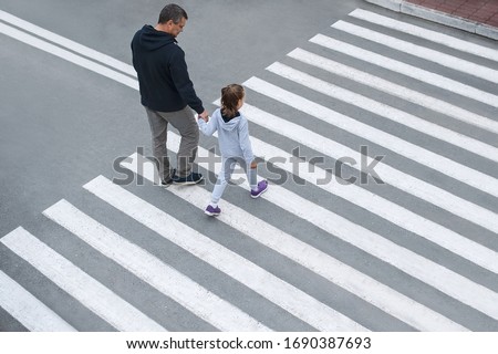 Man and child on a zebra crossing trespassing by crossing the street. In the summer on the street kid girl with her father in fashion clothes cross the road. From top view. Traffic rules for children