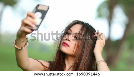 
Beautiful young woman taking selfie of herself with phone. Pretty girl takes selfie outside at park