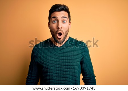 Young handsome man with beard wearing casual sweater standing over yellow background afraid and shocked with surprise expression, fear and excited face. Royalty-Free Stock Photo #1690391743