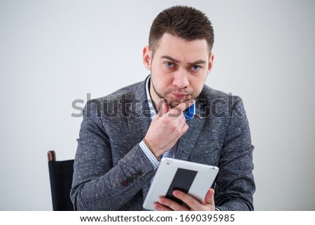Successful business man businessman in a suit sitting on a wooden chair with a tablet and looking at the screen. On a white background with thoughts of a new project