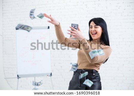 Photo of a charming woman with a smile holding money in her hands and throwing it into the air
