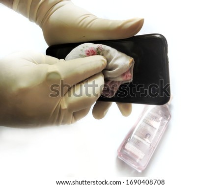 A man wearing hand gloves cleaning his mobile phone with sanitizer in order to avoid viral infection.