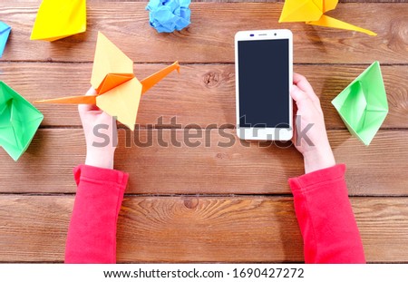 hands of a child with a phone and origami on a wooden table