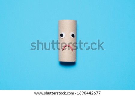 Sad and frowning empty toilet paper roll with googly eyes and mouth on a blue background with copy space and room for text
