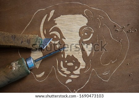 Picture of a dog carved in wood. Next to the painting are the tools used to create it