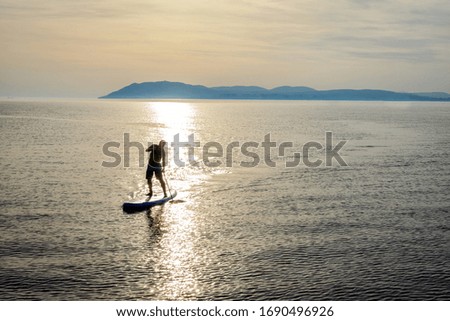 Silhouette of a SUP-rider going by sunshine path on sea surface