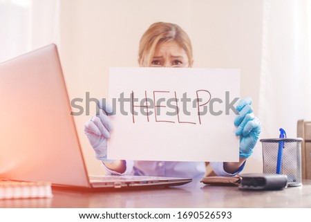 Unhappy Young Businesswoman Holding Flag With The Text Help In Office. Help concept. Virus. Stay home. Woman mask. Problem. Laptop. 
