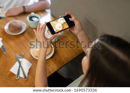 Top view of a young woman taking a photo of some sweet bread and a coffee late in a bakery shop