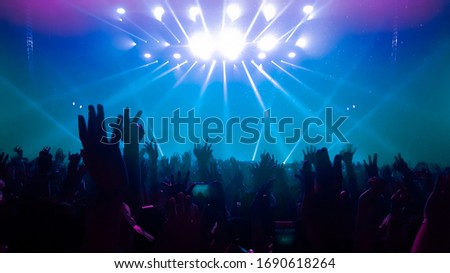 Happy people dance in nightclub DJ party concert and listen to electronic dancing music from DJ on the stage. Silhouette cheerful crowd celebrate New Year party 2020. People lifestyle DJ nightlife.