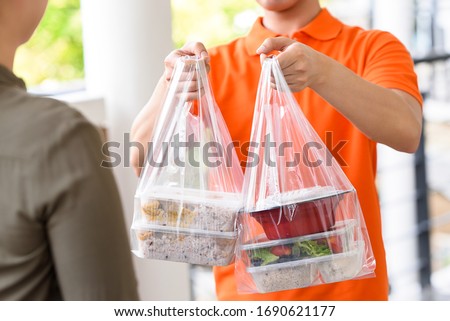Delivery man in orange uniform delivering Asian food boxes in plastic bags to a woman customer at home Royalty-Free Stock Photo #1690621177