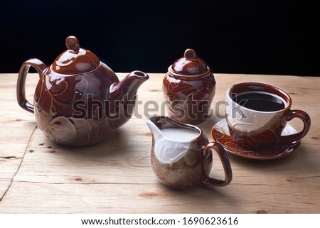 set of teapot, cups, saucers, sugar bowl and milk jug coffee color, in different shots and pictures, yellow wooden table and black background