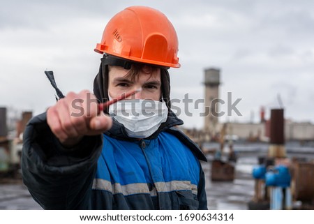 a working fitter in a protective helmet holds a red turn screw in his outstretched hand. The main focus on the turn screw. On the face a protective mask. Action takes place at the factory Royalty-Free Stock Photo #1690634314