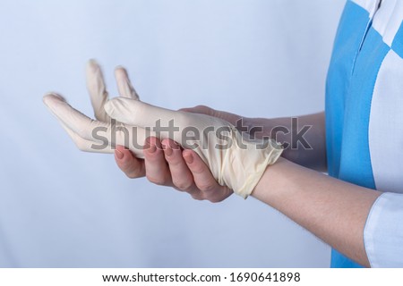 a nurse in uniform puts rubber gloves on her hand. they are designed to protect against microbes, bacteria, diseases, infection with the virus and coronavirus upon contact and shaking hands Royalty-Free Stock Photo #1690641898
