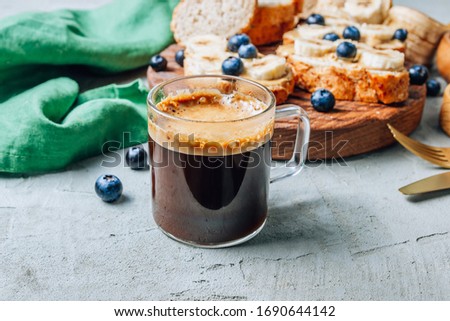 Buckwheat healthy bread with peanut butter, banana and blueberry on wooden board and cup of coffee over concrete background. Selective focus. Summer breakfast.