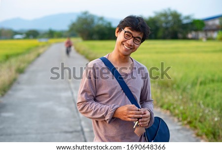 Portrait of an Asian Thai man looking humble and relaxed surrounded by rice field and in the background there is an unknown person riding a bicycle Royalty-Free Stock Photo #1690648366