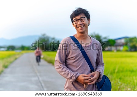 Portrait of an Asian Thai man looking humble and relaxed surrounded by rice field and in the background there is an unknown person riding a bicycle Royalty-Free Stock Photo #1690648369