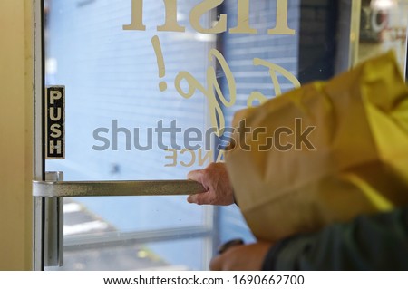 Man pushes the door handle to exit the restaurant after picking up a food order (focus on door)