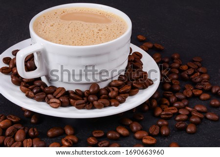 A cup of hot coffee and coffee beans on a black background