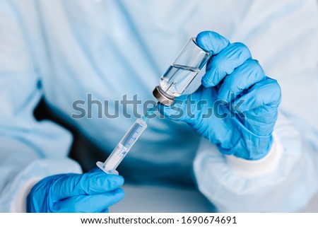 Biological hazard. Epidemic of the Chinese coronavirus. Doctor, nurse, scientist in a protective suit and mask holds an injection syringe and vaccine. Vaccine from, flu, coronavirus, ebola, TB. Royalty-Free Stock Photo #1690674691