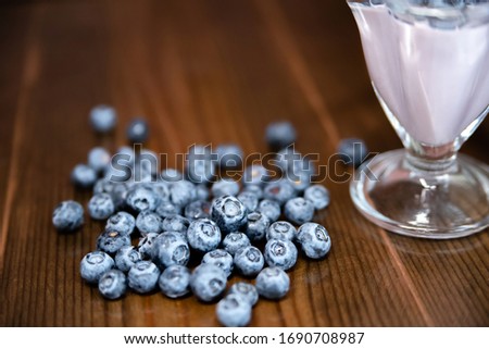 a pile of blueberries on a wooden table next to a bowl of yogurt close-up. healthy diet and delicious Breakfast