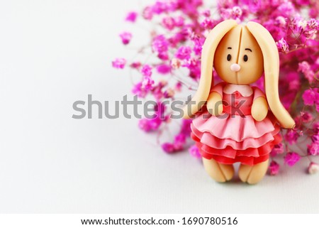 Plasticine Easter Bunny on a blue background. cute Bunny in a beautiful dress next to a bouquet of purple flowers