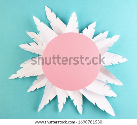 white paper feathers on a blue background, top view. paper decoration with a pink circle on a pastel background