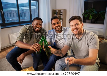 friendship, leisure and people concept - male friends taking picture with selfie stick and drinking beer at home