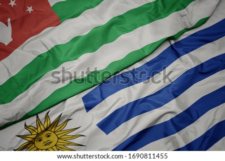 waving colorful flag of uruguay and national flag of abkhazia. macro