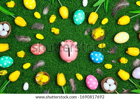 Piggy bank surrounded by eggs and Easter decoration on a green grass background. Saving money for easter holidays.