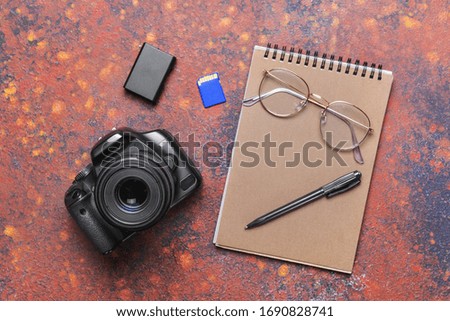 Modern photo camera with notebook, pen and eyeglasses on color background