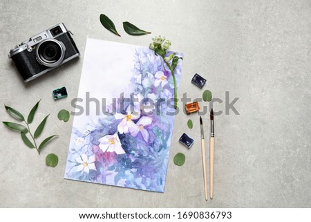 Flat lay composition with watercolor paints and floral picture on grey stone table