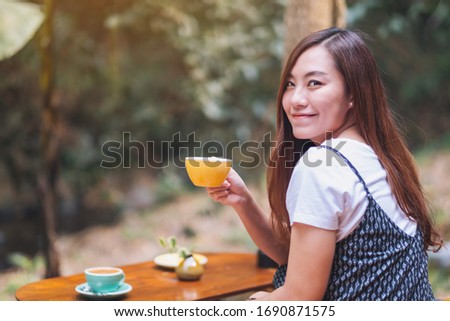 Closeup image of a beautiful asian woman holding and drinking hot coffee in the outdoors