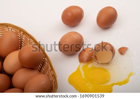 A broken chicken egg, chicken eggs in a wicker basket and chicken eggs scattered on a white background. Close up.