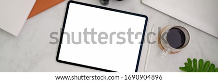 Top view of trendy workspace with blank screen tablet, coffee cup, supplies on marble table   