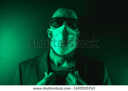 A young Caucasian man with a scarf and sunglasses in the coronavirus pandemic with a green background, Covid-19