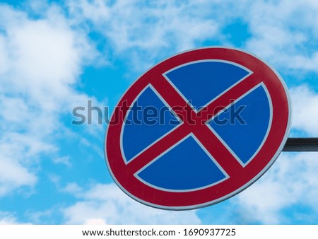 No stopping road sign against a blue sky with white clouds.